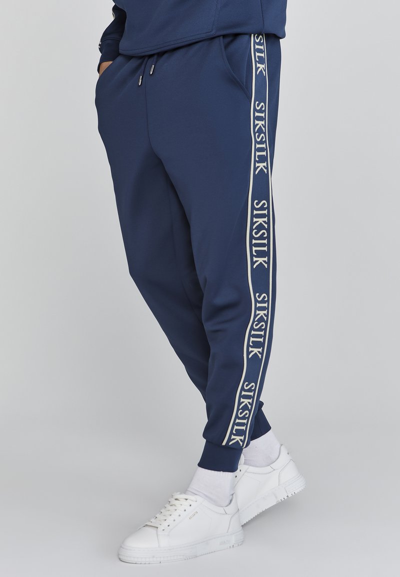 Marine joggers van een lichtgewicht stof met elastische boorden, voorzien van een witte logo-streep aan de zijkant en zakken voor functionaliteit.
