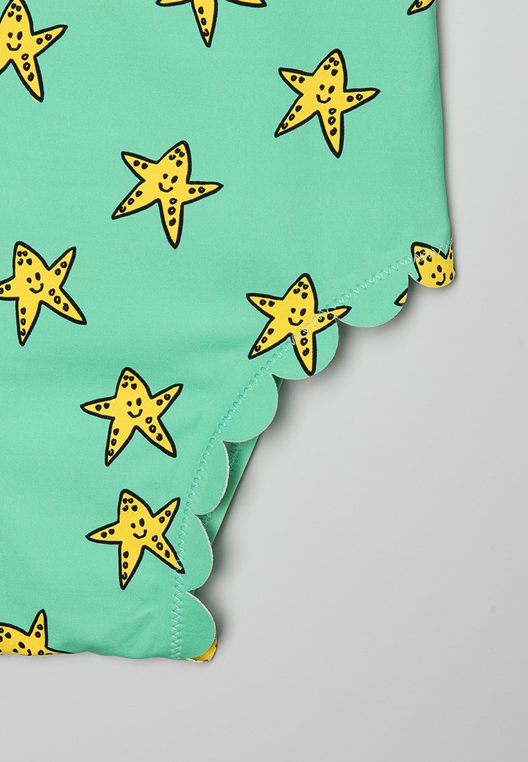 Turkusowy materiał kostiumu kąpielowego w żółty wzór uśmiechniętych rozgwiazd. Posiada falbaniaste krawędzie, gładką teksturę i żywe kolory.