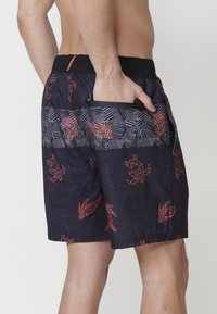 Čierne kraťasy s abstraktným geometrickým vzorom v červenej farbe. Elastický pás, bočná vrecko, ľahký materiál a voľný strih.