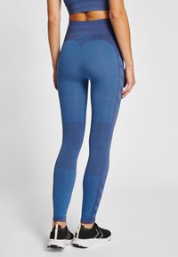 Blå leggings i texturerad tyg, med varierande nyanser och mönster. Hög midja, i kombination med svarta träningsskor.