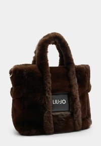Brun faux fur tote taske med to afrundede håndtag, en tekstureret overflade og et logo i sort læder på fronten.