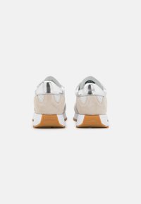 Sneakers con tacco e linguetta in pelle argentata, pannelli in suede beige, suola intermedia bianca e suola esterna in gomma naturale. Dettagli forati inclusi.