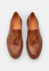 Pantofi slip-on din piele maro, cu o textură netedă, accente din ciucuri și vârf rotunjit. Interiorul este de culoare portocalie, cu o marcaj subtil.