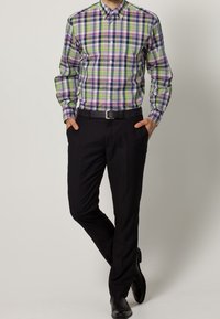 Långärmad, rutigt skjorta med gröna, lila och blå mönster, matchad med svarta byxor och ett svart bälte, bärs med svarta skor.