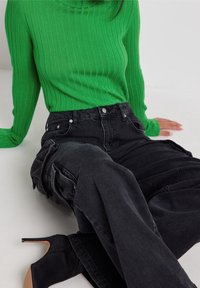 Pull vert côtelé à manches longues assorti à un pantalon cargo noir taille haute avec des poches et une coupe ample, complété par des bottines à talons noires.