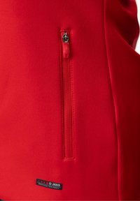 Rode sportieve zip-up jas met een kleine zak met een zilveren rits en een zwart logo-label dichtbij de zoom. Zachte, gladde textuur.