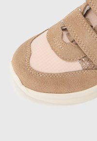 Baskets en daim beige avec un panneau en mesh rose clair et des accents pailletés. Dotées d'un design courbé et d'une fermeture à scratch pour un enfilage facile.