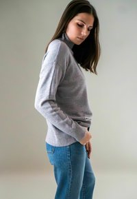 Lichtgrijze trui met een hoge hals, geribde manchetten en een ontspannen pasvorm, gecombineerd met blauwe spijkerbroek. Zachte textuur, casual ontwerp.