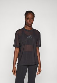 Zwarte mesh sport t-shirt met ronde hals, korte mouwen en een logo aan de voorkant met drie strepen. Gecombineerd met donkere leggings.