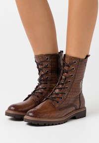 Bottes de combat montantes marron en cuir texturé à motif crocodile. Elles disposent de semelles en caoutchouc robustes et d'œillets métalliques pour les lacets.