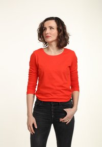 Maglietta rossa a maniche lunghe in cotone con scollatura rotonda, abbinata a jeans neri a vita alta con chiusura frontale a bottoni.