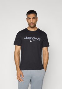 Sort bomulds T-shirt med "Just Do It" tekst og Nike-logo i kontrasterende hvid og blå. Korte ærmer, rund halsudskæring.