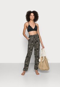 Zwarte triangelsupport bh gecombineerd met hoge taille, gestreepte, wijde broek in zwart en crème, met zakken en een beige handtas.