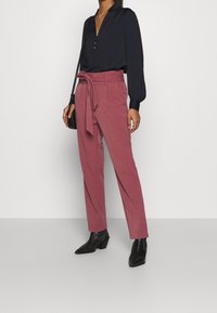 Navy blouse met een V-hals en knoopsluiting, gecombineerd met roze high-waisted broek met een strikriem en zwarte enkellaarsjes met blokhak.