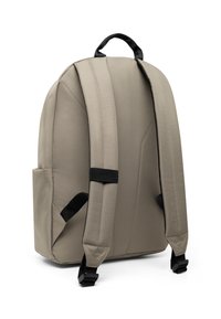 Beige ryggsäck med vadderat tyg, justerbara svarta remmar, sidofack och ett handtag på toppen. Slät textur med sömlös design.