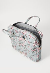 Laptop torba s cvjetnim uzorkom u svijetloplavoj boji, sa zatvaranjem na patentni zatvarač, dvostrukim ručkama i siva unutrašnjost. Sadrži naglaske od zlatnog metala.