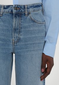 Light blue denim jeans with a high waist, classic five-pocket design, and visible stitching details. The fabric appears soft and textured.