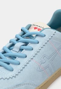Ανοιχτό μπλε σουέτ αθλητικά παπούτσια με υφή, μυτερή μύτη, επίπεδες κορδόνες και ροζ διακοσμητικές ραφές. Διαθέτουν ετικέτα μάρκας στη γλώσσα.