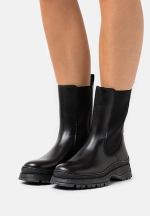 Black leather ankle boots with elastic side panels, rounded toes, and thick rubber soles featuring a textured tread for grip.