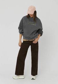 Sweatshirt gris avec le texte "OUTSIDE", superposé à un haut beige. Pantalons large en velours côtelé marron et casquette rose clair. Des baskets blanches complètent le look.