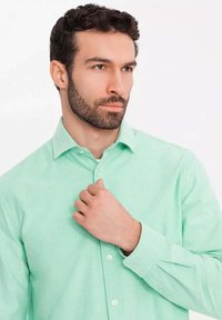 Camicia verde menta con bottoni in tessuto morbido, caratterizzata da maniche lunghe, colletto e vestibilità slim. La texture della camicia appare liscia e fine.