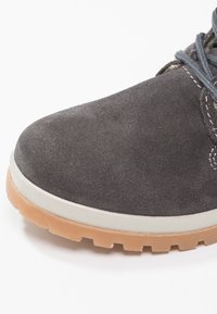 Chaussure en daim gris avec un bout arrondi, une surface texturée et une semelle claire dotée d'une semelle épaisse à motif. Lacets de couleur contrastante.