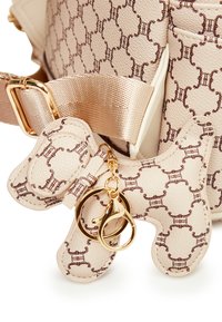 Beige läderväska tag formad som en hund, med ett brunt mönster och guldfärgad hårdvara. Fäst vid ett satinband på en väska.