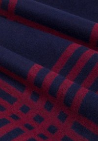 Wełniany koc o ciemnoniebieskim tle i czerwonym wzorze kratki, z poziomymi i pionowymi liniami, miękką teksturą oraz złożonymi warstwami.