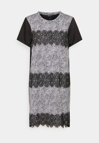 Černobílé šaty s krátkým rukávem, které mají skvrnitý vzor a krajkový detail na hrudi, s okrajem ve tvaru vlny.