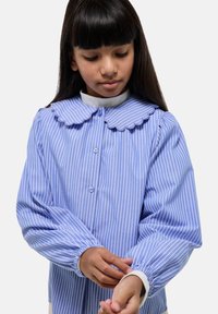 Blouse rayée bleue avec un col en forme de feston, des manches bouffantes longues et des boutonnages. Texture douce en coton avec des poignets élastiques.