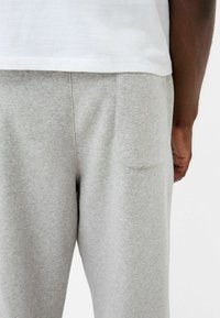 Helle graue Jogginghose aus weichem Baumwollgemisch, mit einer Gesäßtasche und einer lässigen Passform, kombiniert mit einem schlichten weißen T-Shirt.