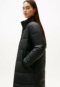 Schwarze Daunenjacke mit hohem Kragen, ausgestattet mit horizontalem Steppmuster, Seitentaschen und einem Reißverschluss vorne, aus glänzendem Material gefertigt.