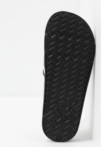 Zwarte rubberen sandalenzool met een zigzagprofiel en een reliëflogo. Glad afgewerkte randen met een iets verhoogd ontwerp voor betere grip.