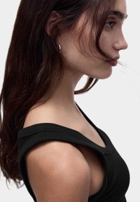 Débardeur noir à côtes avec de larges bretelles. Présente un décolleté arrondi et une silhouette ajustée, mettant en valeur un tissu lisse et texturé.