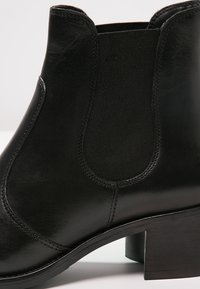 Zwarte leren enkellaars met elastische zijpanelen, ronde neus en gestapelde hak. Glad oppervlak met gestikte accenten.