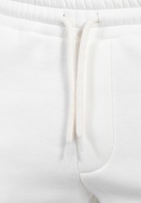 Pantalones deportivos blancos con tejido texturizado, cintura elástica y cordón plano con detalles acanalados. Incluye bolsillos laterales.