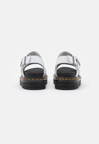 Weiße Ledersandalen mit zwei verstellbaren Riemen, schwarzen Gummisohlen und kontrastierenden orangefarbenen Nähten entlang der Sohle.