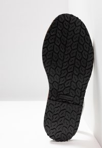 Semelle de chaussure avec une bande de roulement en caoutchouc noir texturé présentant un motif géométrique rappelant des galets et un marquage du numéro de taille.
