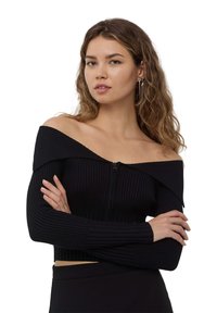 Top corto nero a costine con design off-the-shoulder e zip frontale. Le maniche lunghe e il tessuto texturizzato creano una silhouette aderente.