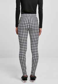 Leggings à motif pied-de-poule noir et blanc avec une taille haute et une silhouette ajustée, assortis à des chaussures noires.