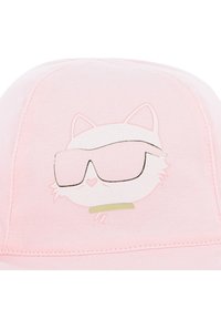 Ροζ καπέλο με γραφικό λευκής γάτας που φοράει μεγάλα γυαλιά ηλίου και μεταλλικές πράσινες λεπτομέρειες, τονίζοντας μια απαλή βαμβακερή υφή.