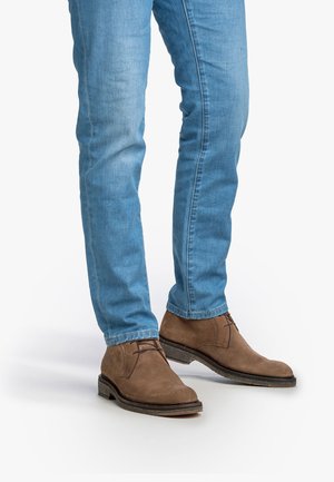 Bruine suède chukka boots met een gestructureerd oppervlak en vetersluiting, gecombineerd met lichtblauwe slim fit jeans.