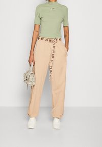 Světle zelené vypasované tričko s krátkým límcem, v kombinaci s béžovými volnými kalhotami s páskem s logem Nike a neformálními bílými teniskami.