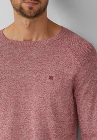 Rot meliertes Strickpullover mit rundem Halsausschnitt und strukturierten Schultern. Enthält ein kleines Logo auf der Brust. Weiches, lässiges Design.