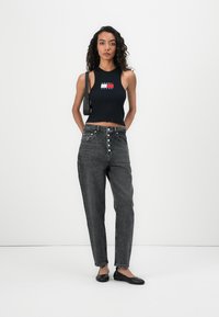 Black ribbed crop top with logo detail paired with high-waisted, faded black jeans featuring button closure and straight-leg cut. Black flats.
