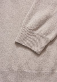Hellbeiger Pullover mit einer gestrickten Textur, gerippten Bündchen und Saum, mit einem glatten Stoff, der zu einem dezenten, weichen Finish übergeht.