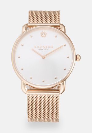 Montre ronde avec un cadran blanc, accents en or rose et bracelet en maille. Présente des marqueurs en points minimalistes et un emblème de fleur sur la couronne.