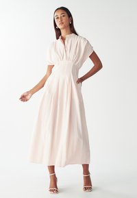 Heled roosa triibuline kleit, millel on krae, lühikesed puhv-sleeved, vöökoht ja voolav seelik, valmistatud siledast materjalist. Hõbedased kontsakingad.