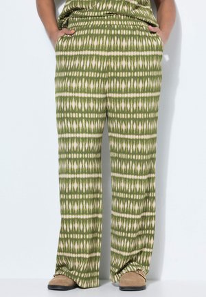 Groen-wit patroon wijde broek met beige suède schoenen, handen in de zakken, staand tegen een witte achtergrond.