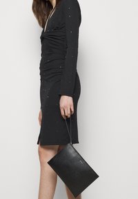 Robe noire à manches longues avec des détails froncés et des strass dispersés. Pochette en cuir noir avec fermeture éclair et bandoulière.